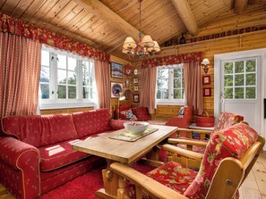 L’intérieur d’un chalet accueillant, avec un plafond en bois, des rideaux à motifs rouges, une table en bois et un canapé rouge.