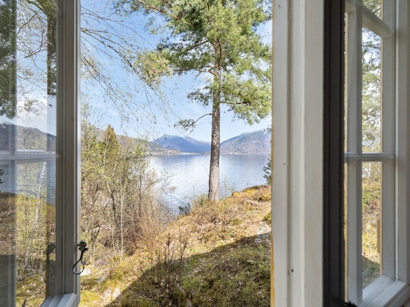 A view through an open window of a lake with mountains in the background.