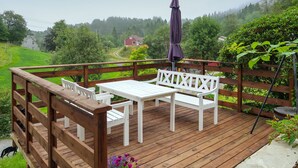 Une terrasse en bois avec une table et un banc blancs, entourée d’une balustrade en bois.
