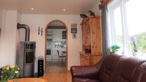 Un salon chaleureux avec un canapé en cuir, une cuisine à l’arrière-plan et un meuble en bois sur lequel est posé un oiseau.