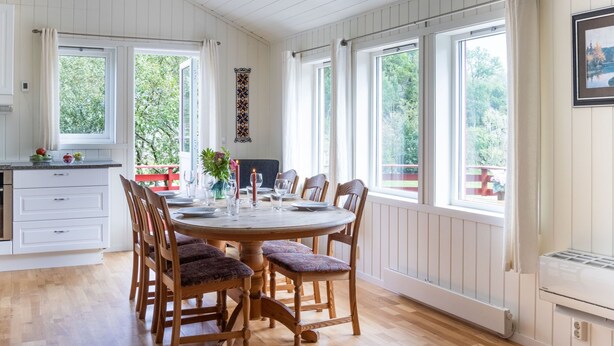 A dining area with a round wooden table, six chairs, and a view of greenery outside. - Fjordglytt by Interhome (Onarheim)