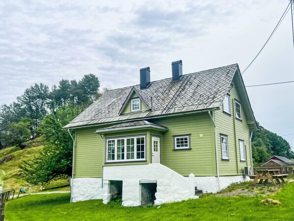 A two-story house with a steeply pitched roof, white exterior walls, and a small front porch.