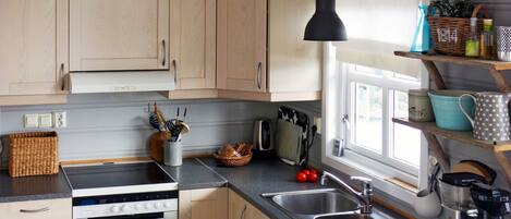 A kitchen with light wooden cabinets, a black countertop, a Bosch oven, a sink, and a coffee maker.