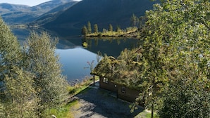 A cabin with a gravel path leading to a lake, surrounded by trees and mountains.