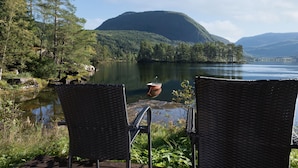 A lakeside view with wicker chairs facing the water, surrounded by forested hills.