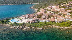 Vue aérienne d’un quartier résidentiel situé sur la côte, avec des maisons, une mer d’un bleu éclatant et une piscine.