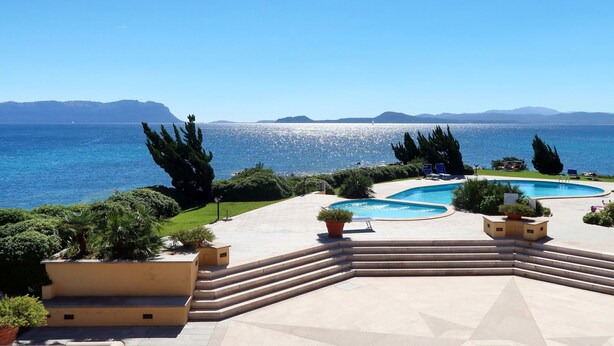 A pool area with steps leading to the water, surrounded by greenery and overlooking a large body of water with distant mountains. - Apartment Timo by Interhome (Golfo Aranci)