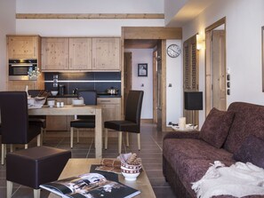 Un soggiorno moderno con un divano marrone, un tavolo da pranzo con sedie e una zona cucina con pensili in legno e un piano di lavoro nero.