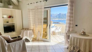 Ein Wohnzimmer mit Fernseher, einer Couch und einem Balkon mit Tisch und Stühlen.
