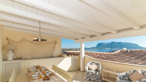 A covered outdoor dining area with a table set for two, a chair, and a hanging light fixture.