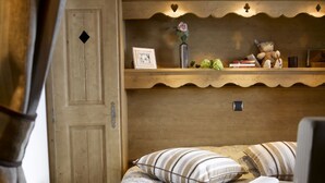 Une chambre confortable avec une tête de lit en bois, un lit recouvert d’une literie à motifs floraux, une table de chevet avec une lampe et une étagère ornée d’objets décoratifs.