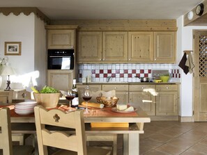 Cucina con mobili in legno, zoccolo paraschizzi in ceramica e zona pranzo con tavolo apparecchiato per due.