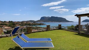 A patio with two blue sun loungers, a stone wall, and a view of the sea and mountains. - Lentischio by Interhome (Golfo Aranci)