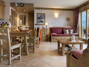 A cozy living room with a wooden dining table, a sofa, and a view of the outdoors through a large window.