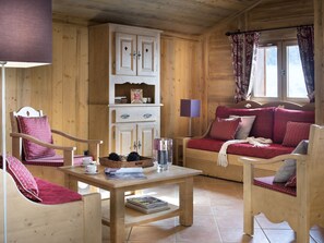 Interior acolhedor de uma cabana de madeira, com um sofá, cadeiras, uma mesa e um armário.