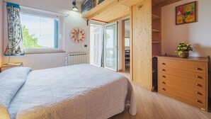 A bedroom with a bed, a dresser, a window with curtains, a radiator, and a door leading to an outdoor area. - Casa Marepietra by Interhome (Lerici)
