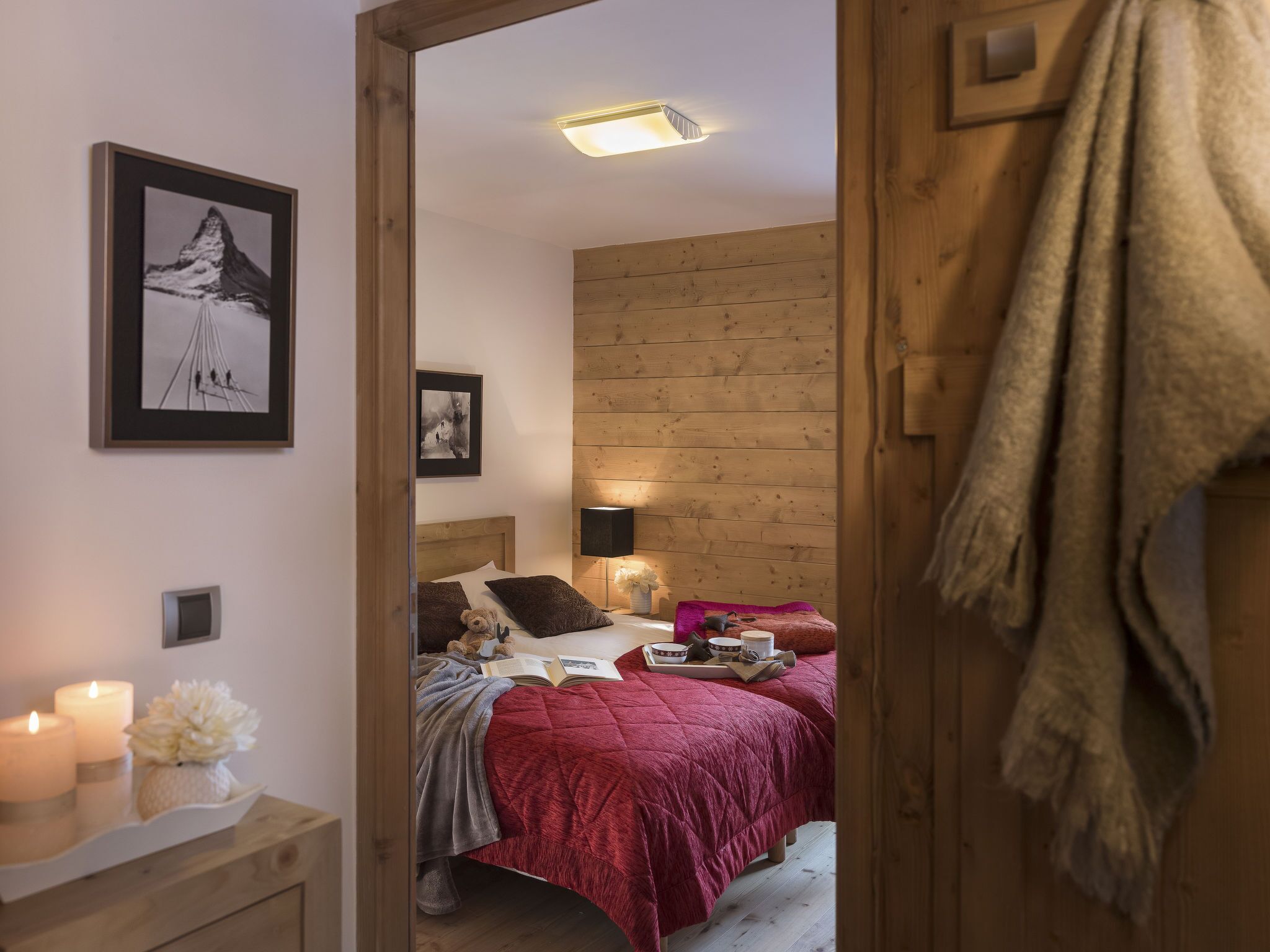 Un dormitorio acogedor con cabecera de madera, una cama con colcha roja, una mesita de noche con velas y un cuadro enmarcado en la pared.