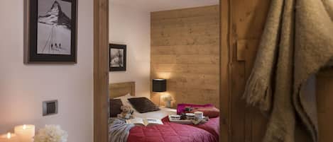 Un dormitorio acogedor con cabecera de madera, una cama con colcha roja, una mesita de noche con velas y un cuadro enmarcado en la pared.