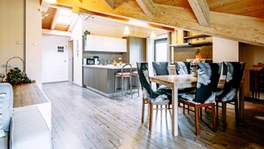 Un comedor espacioso con una mesa y sillas de madera, una cocina al fondo y un techo alto con vigas a la vista.