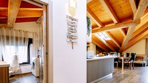 Un loft espacioso con techo alto, vigas de madera, una zona de cocina y un área de descanso con sofá y sillones.
