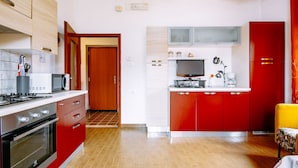 Una cocina moderna con gabinetes rojos, un microondas, una estufa y un televisor.
