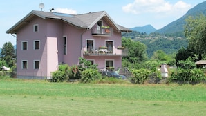 Una casa rosa de dos pisos con balcón, rodeada de campos verdes y montañas.