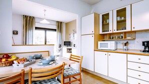 Eine Küche mit Esstisch, Stühlen, einer Mikrowelle, Schränken und einem Fenster mit Vorhängen.