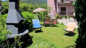 Eine Terrasse mit einem Steingrill, einem blauen Klappstuhl und einem bunten Sonnenschirm.