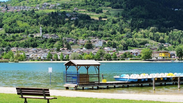 Blick auf einen See mit einer Holzsteganlage, einer Bank und einer Reihe von Booten.