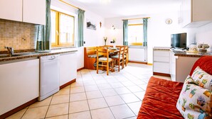 A compact kitchen with a dining area, a TV, and a red couch. - Stabler by Interhome (Pozza di Fassa)