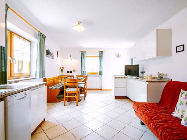 Un espace de vie compact comprenant une cuisine, un coin repas et un canapé rouge.