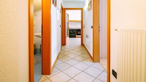 Un pasillo con puertas de madera, suelo de baldosas y una cocina al fondo.