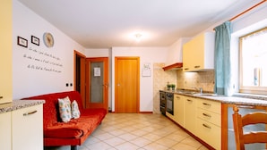 Una cocina compacta con un sofá rojo, una mesa de comedor de madera y una ventana con cortinas.