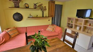 Een woonkamer met een bank, een houten tafel, een televisie en decoratieve objecten op planken.