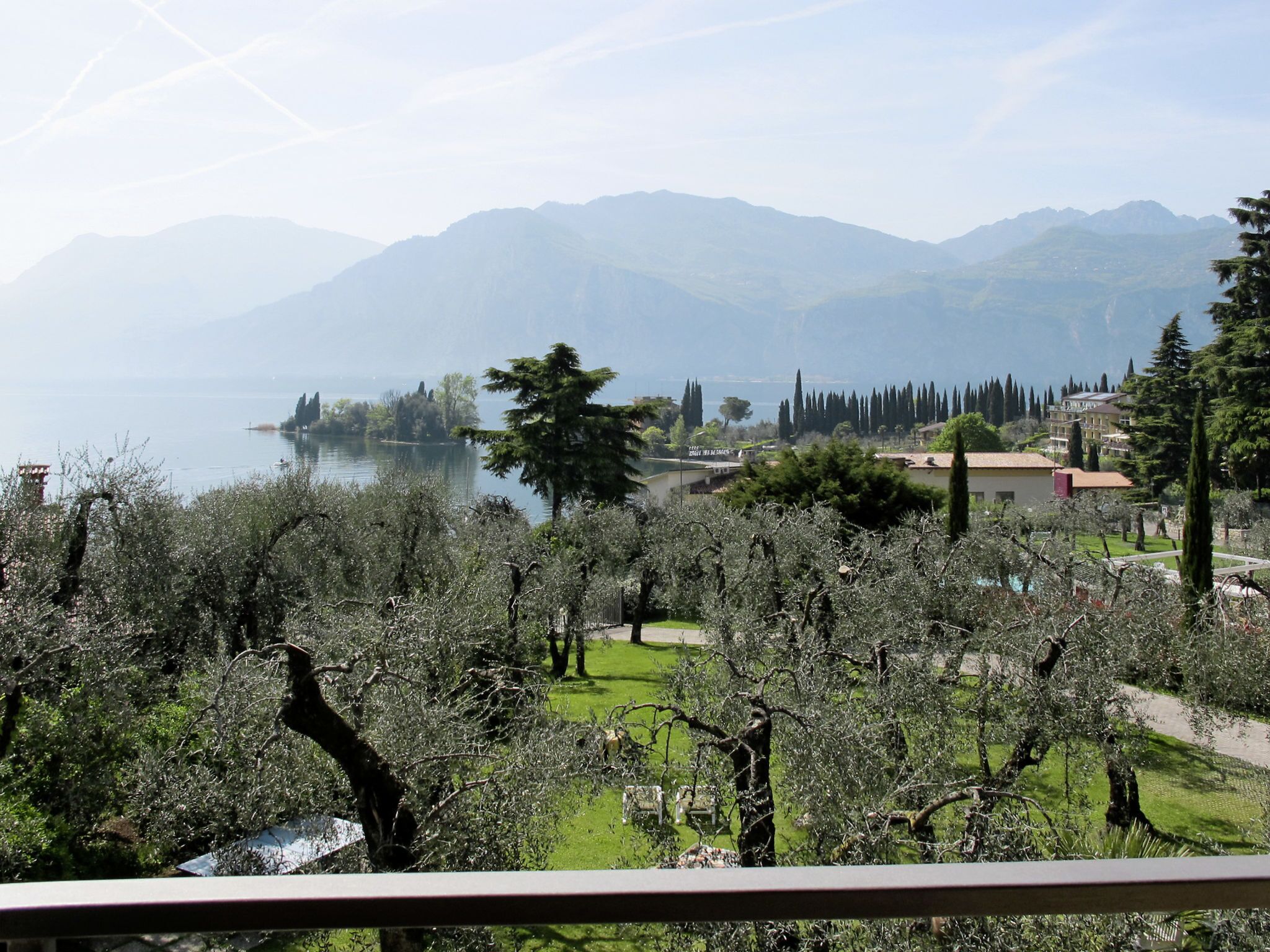 A lakeside view with mountains in the background, a grassy area with trees, and buildings along the shore.
