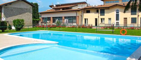A swimming pool with a clear blue water surface, surrounded by a well-maintained lawn and a building with a tiled roof.