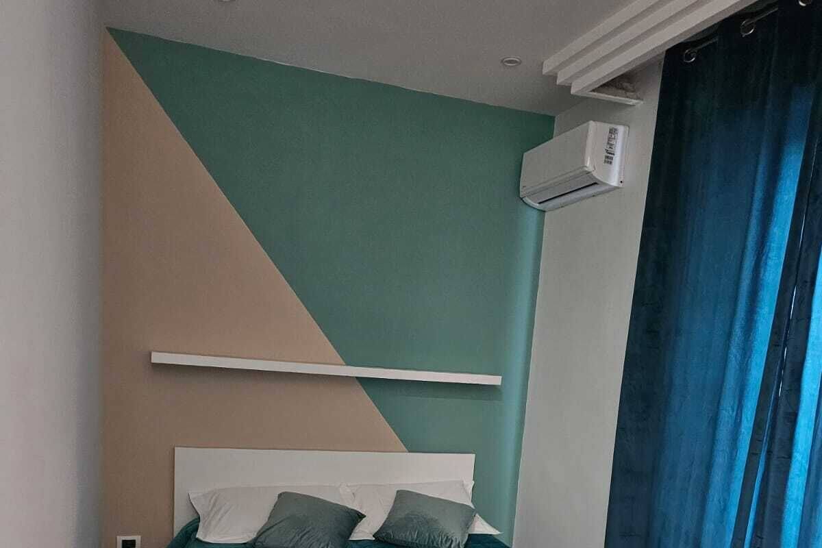 A bedroom with a bed, a wall-mounted air conditioner, and a window with curtains.