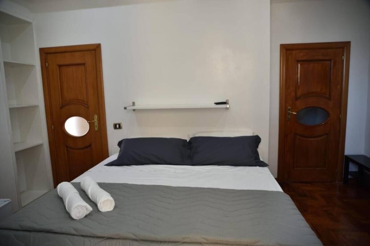 A bedroom with a bed, two wooden doors, a white shelf, and a towel on the bed.