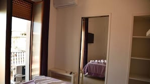 Een hotelkamer met een bed, nachtkastje, spiegel, kledingkast en een balkon met een hekwerk.