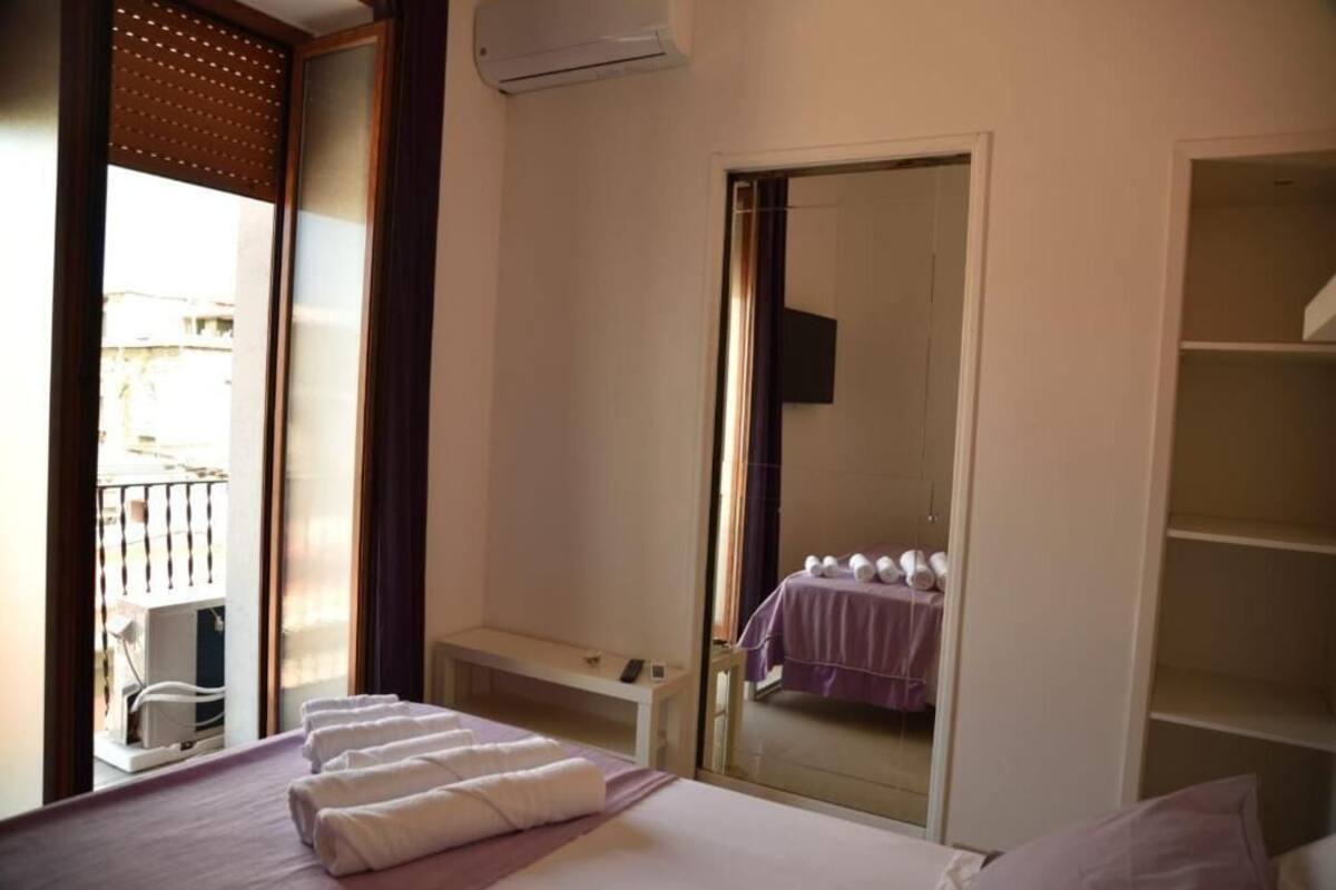A hotel room with a bed, a bedside table, a mirror, a wardrobe, and a balcony with a railing.