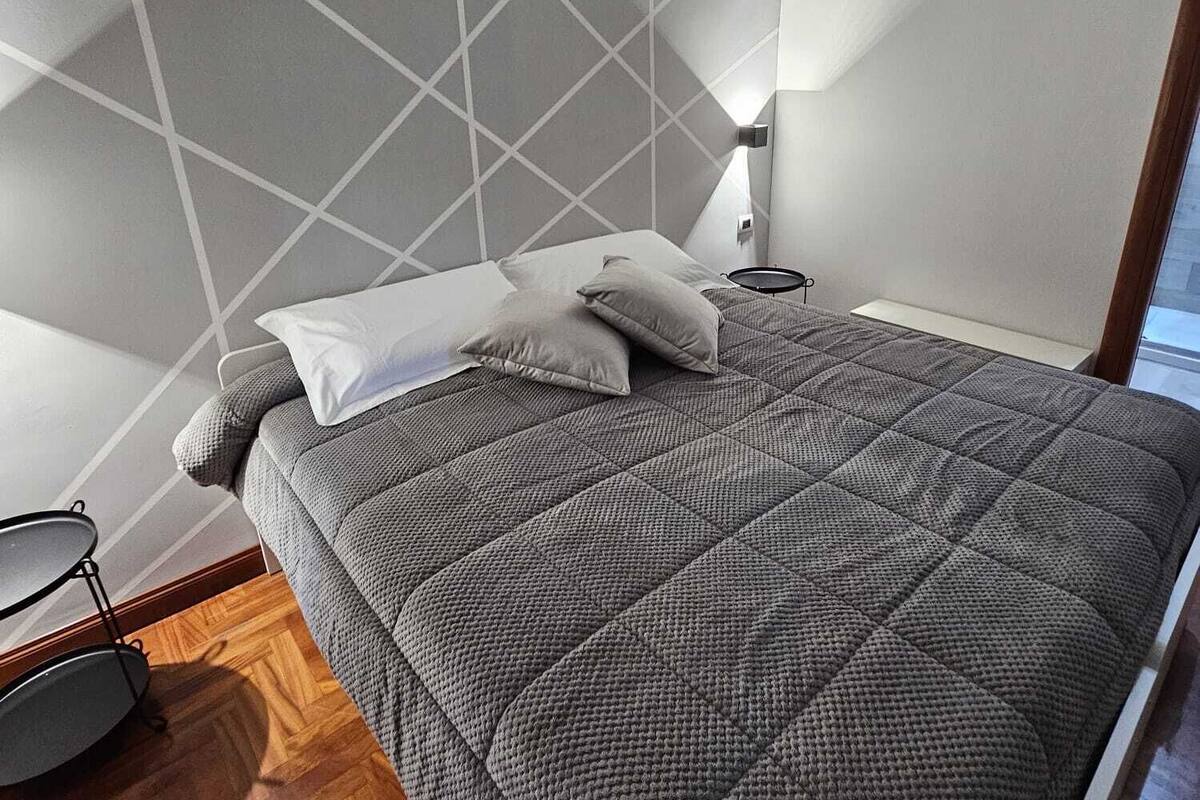 A bedroom with a bed, pillows, a bedside lamp, and a wooden floor.