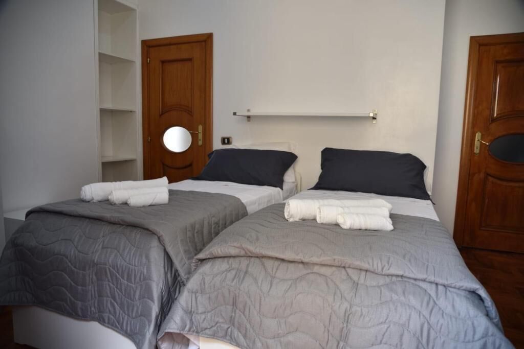 A room with two beds, each with a grey quilt and white pillows, and a wooden door with a circular mirror.