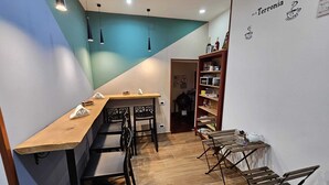Een eethoek met een lange houten tafel, zwarte stoelen en hanglampen. Tegen de muur staat een boekenkast met diverse objecten.