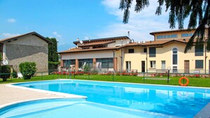 A swimming pool with a clear blue water surface, surrounded by a well-maintained lawn and a building with a tiled roof. - Il Colombaro by Interhome (Salo')