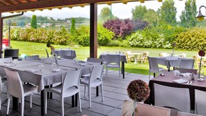 An outdoor dining area with tables and chairs, a covered roof, and a view of a garden and trees. - Il Colombaro by Interhome (Salo')