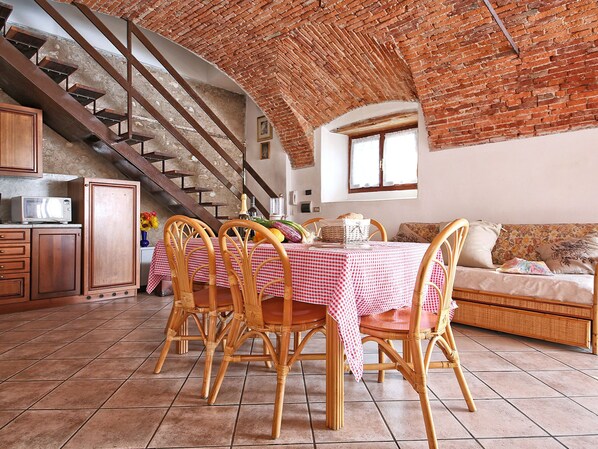 Un coin repas avec une nappe à carreaux, des chaises en osier, un plafond en briques et un escalier.