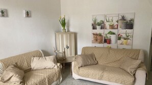 A living room with two beige couches, a cabinet with potted plants, and a wall-mounted plant display. - The five olive trees (Alberobello)