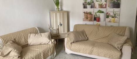 A living room with two beige couches, a cabinet with potted plants, and a wall-mounted plant display.