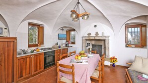 A kitchen with a dining area, featuring a tiled floor, wooden cabinets, a stove, and a fireplace. - Il Colombaro by Interhome (Salo')