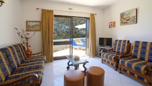 A room with two plaid sofas, a small table, and a television. There is a large sliding door leading to an outdoor area with a pool and umbrellas.
